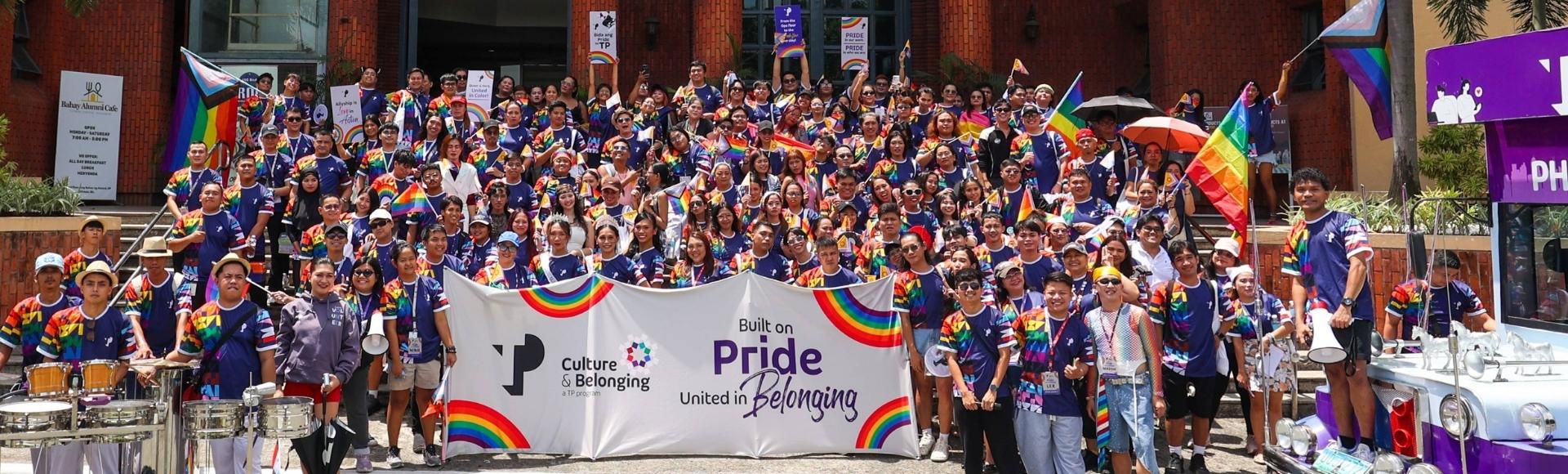 TP employees in front of a building posing and showing a banner with the words, Built on Pride, United in Belonging