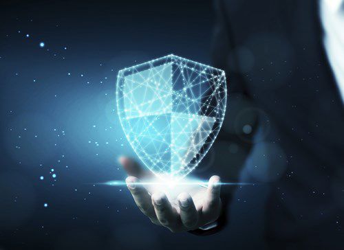 A holographic shield hovers above an open hand, glowing with light, in a dark, digital environment with subtle blue accents.