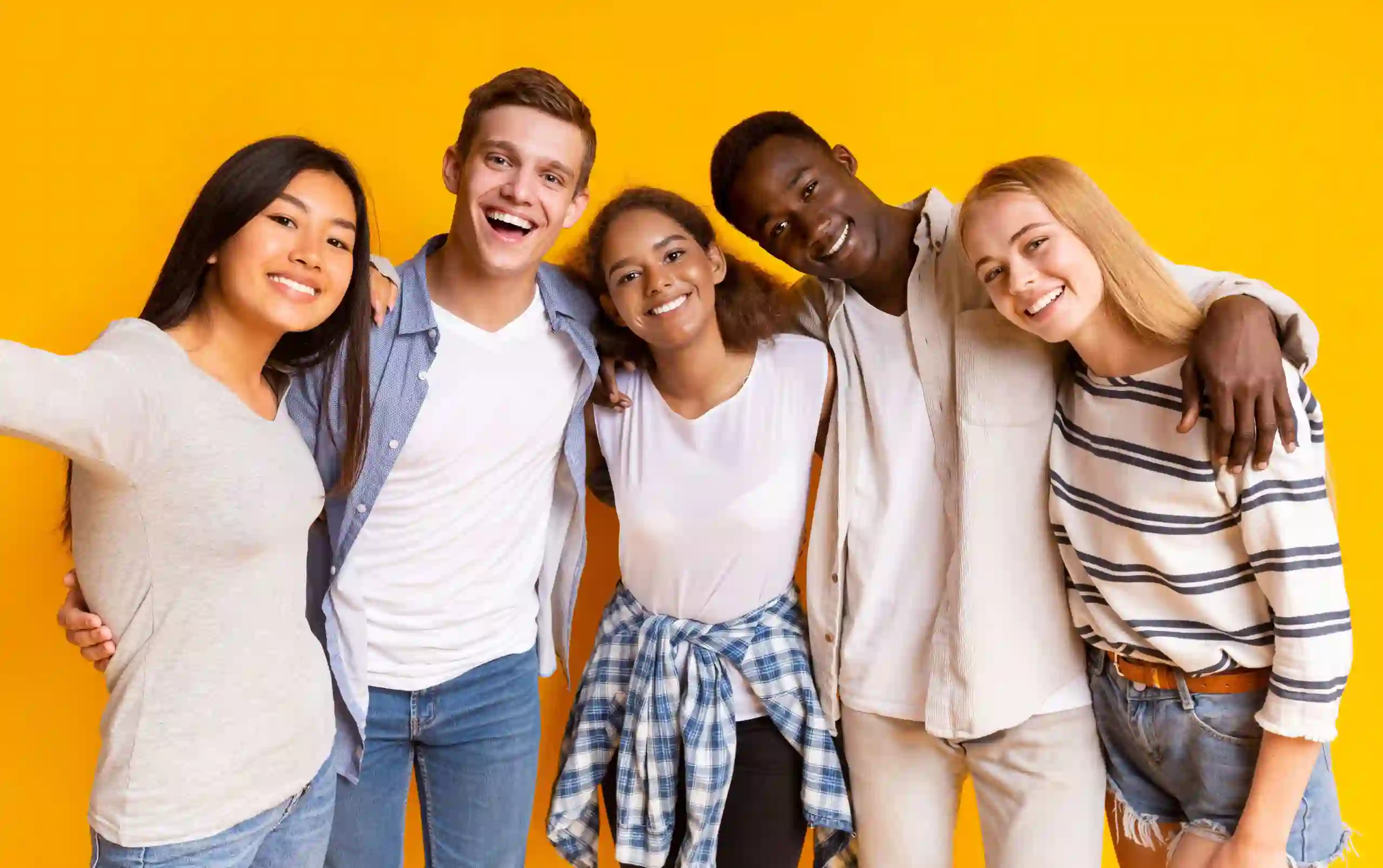 Group of diverse young friends smiling and standing together against a yellow background