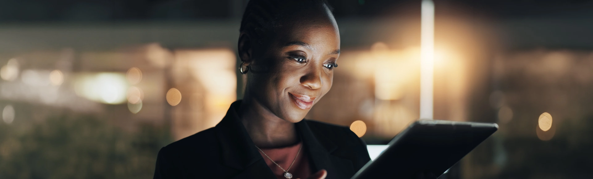 Professional using a tablet at night with city lights in the background.