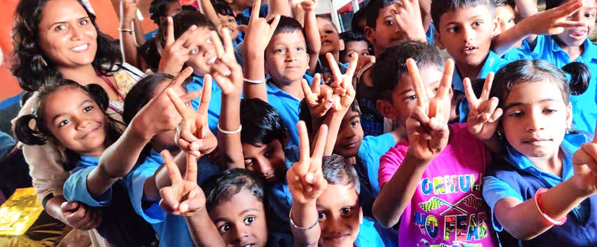 Group of children smiling and raising their hands in peace signs, wearing colorful clothes.