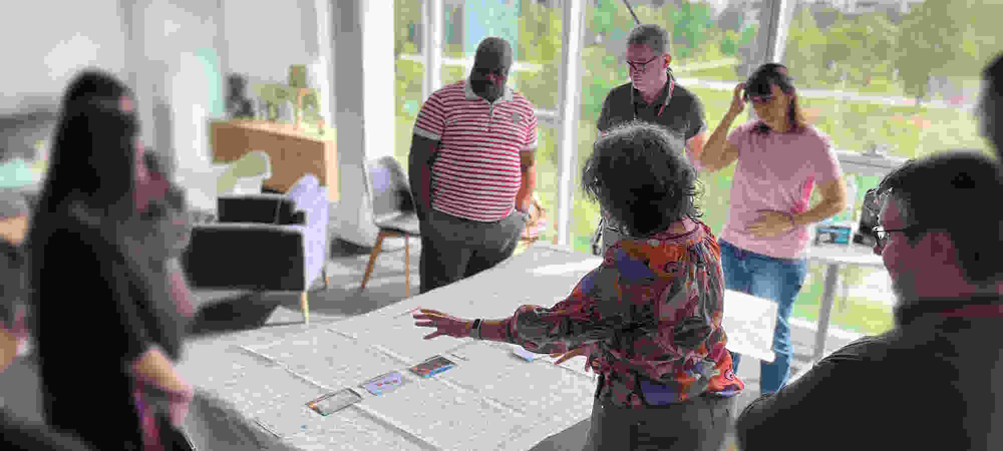 Un groupe échange autour d’une table avec des cartes, dans un bureau lumineux et convivial.