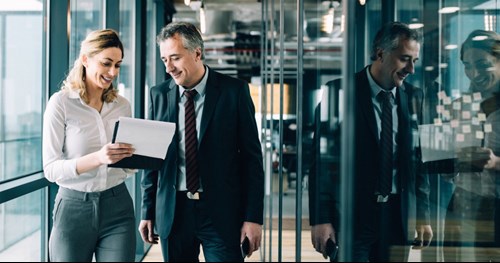 Business couple analyzing team results on a tablet in a glass-walled office