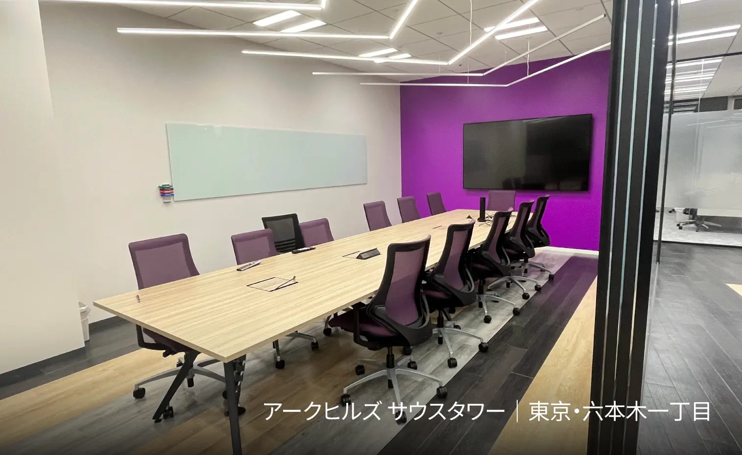 The meeting room has a long table, several chairs and a projection TV. There is also a writing board on the wall.