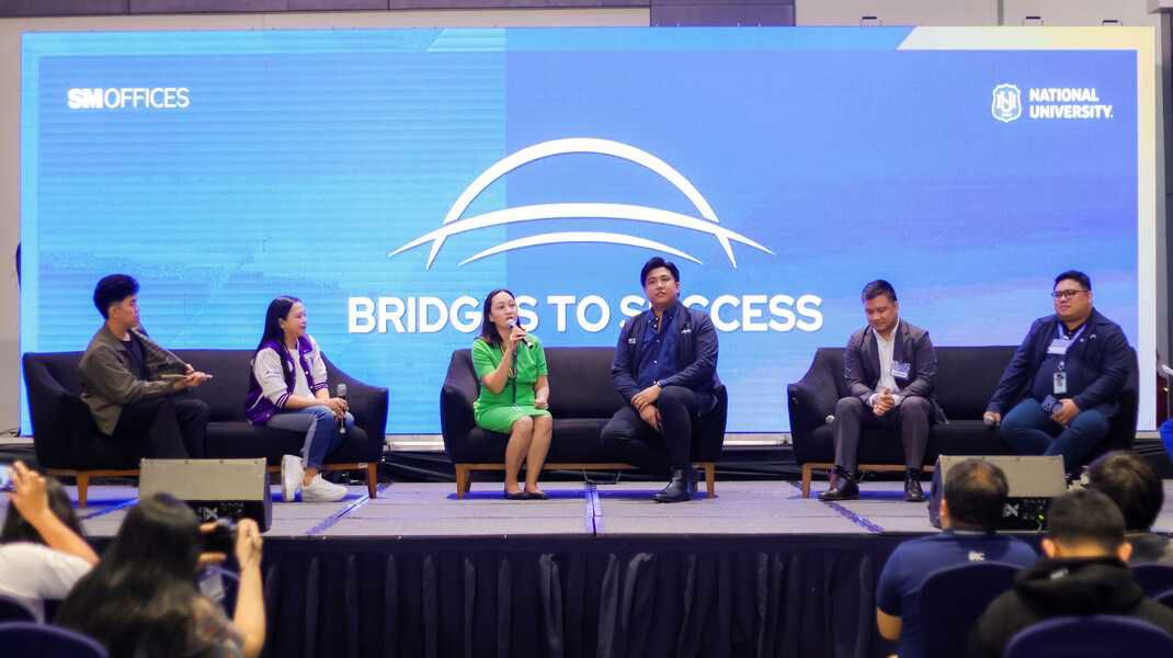 Six people on stage during the Bridges to Success event. TP female employee is holding the mic and speaking.