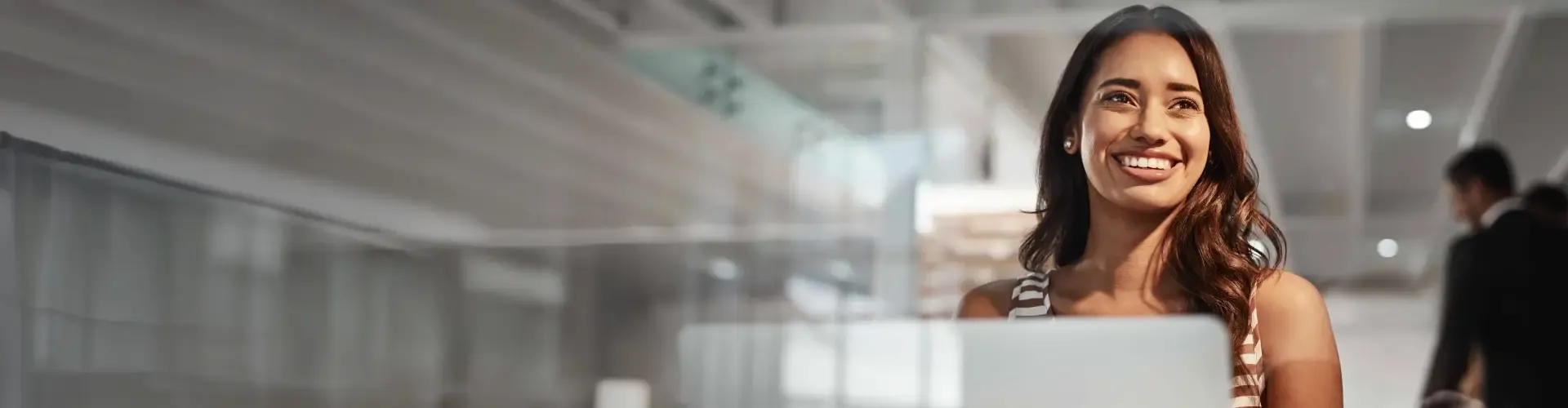 Smiling woman working on her laptop on a modern glass wall office