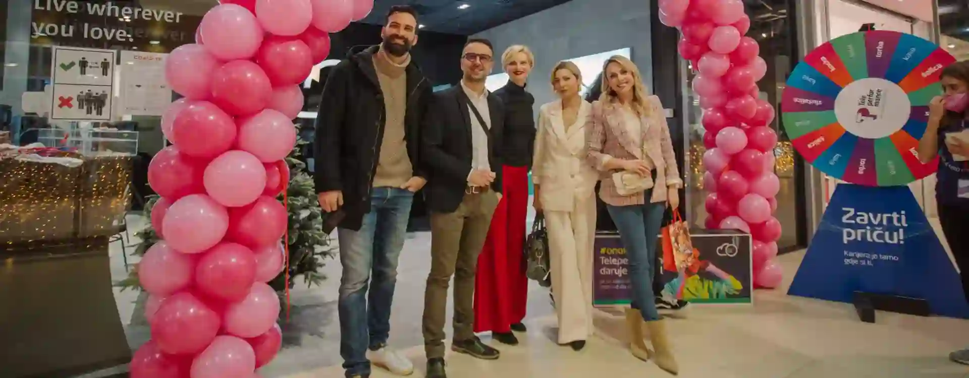 A group of people standing and smiling at a festive indoor event, framed by pink balloon arches