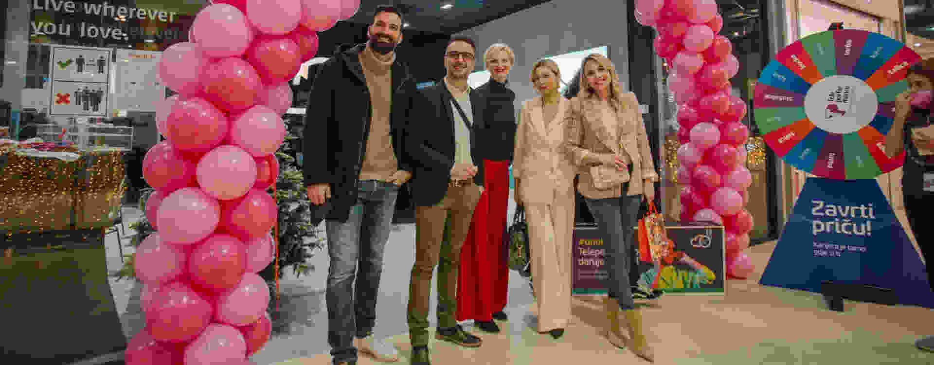 A group of people standing and smiling at a festive indoor event, framed by pink balloon arches