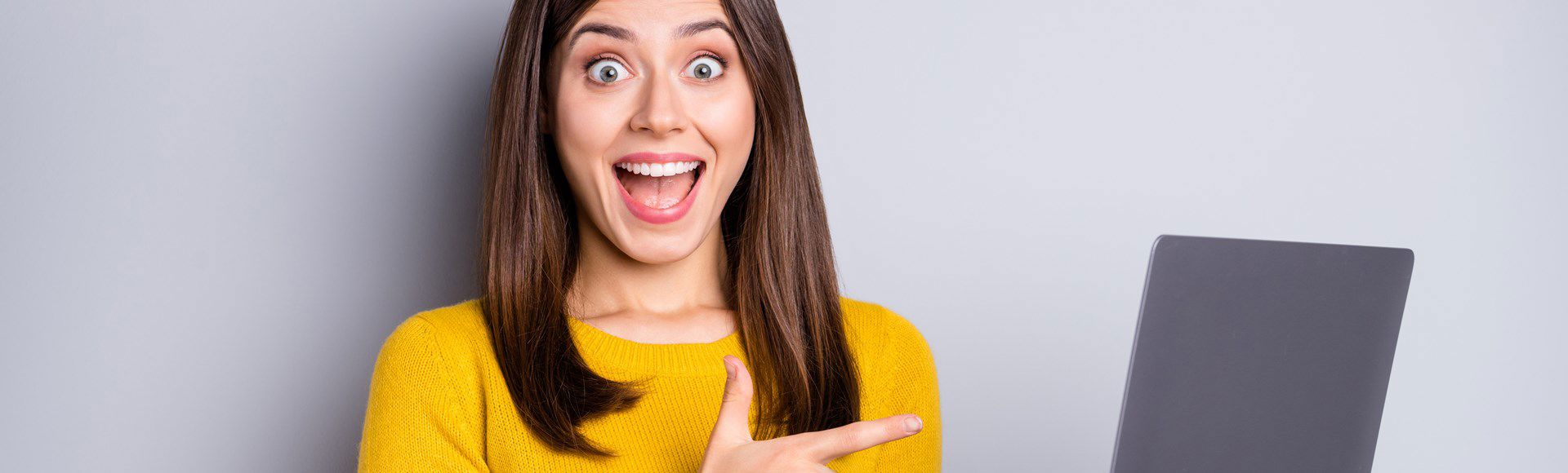 Surprised young woman pointing excitedly at something amazing on her laptop screen.