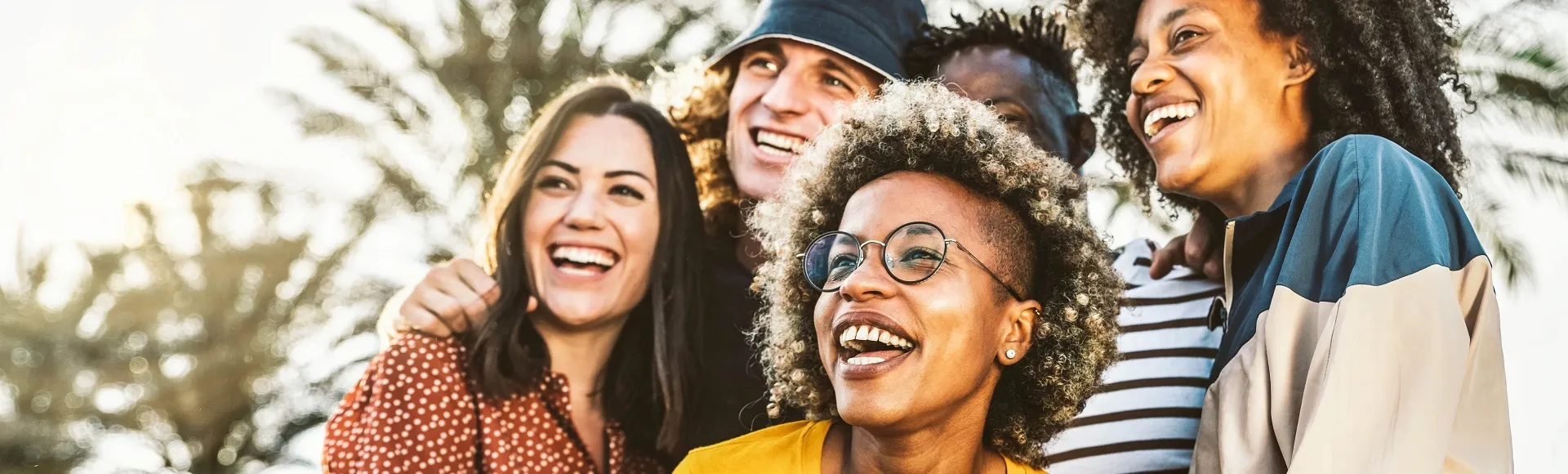 Group of friends laughing together outdoors in a sunny park.