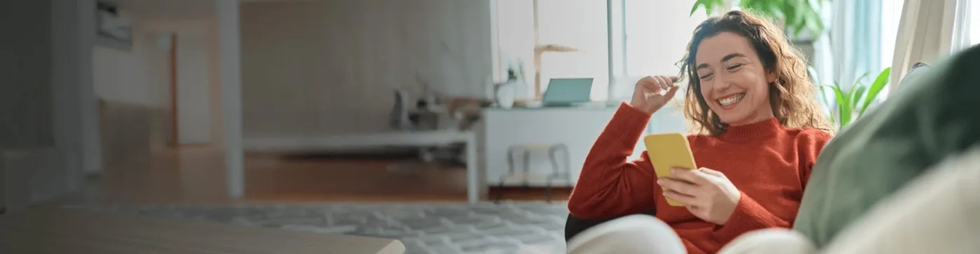 Smiling woman sitting comfortably on her sofa and browsing her cellphone