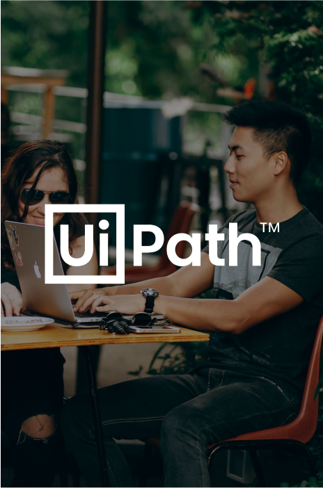 UiPath logo in focus and a couple using their laptops in the background UiPath logo in focus and a couple using their laptops in the background