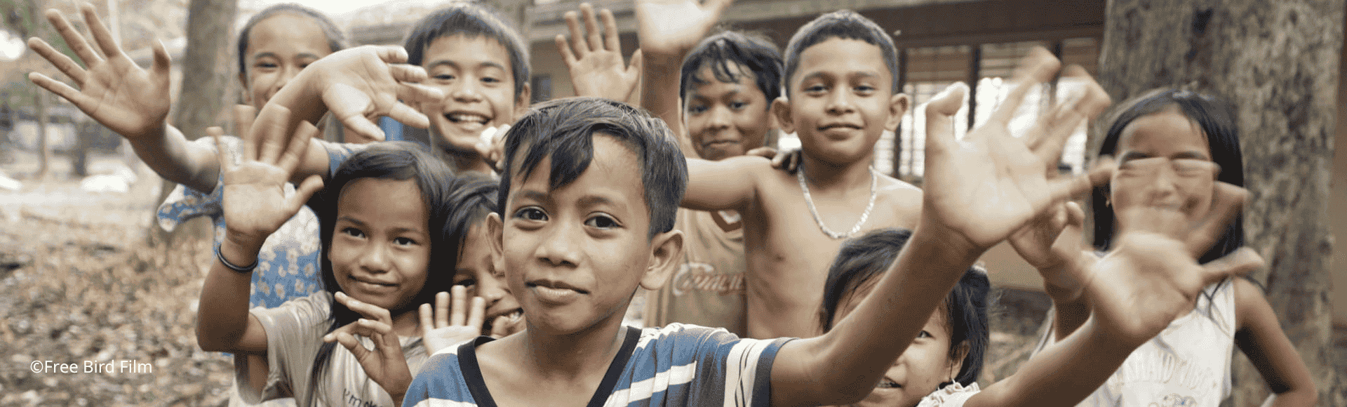 Children supported by the TP and UNICEF partnership smiling and waving at the camera.