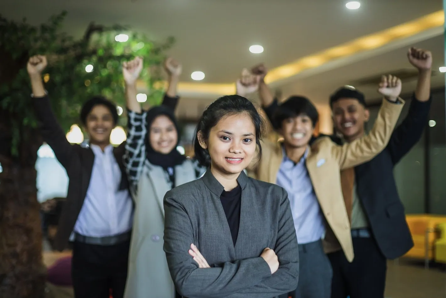 Confident professional standing in front while team members celebrate success in the background.