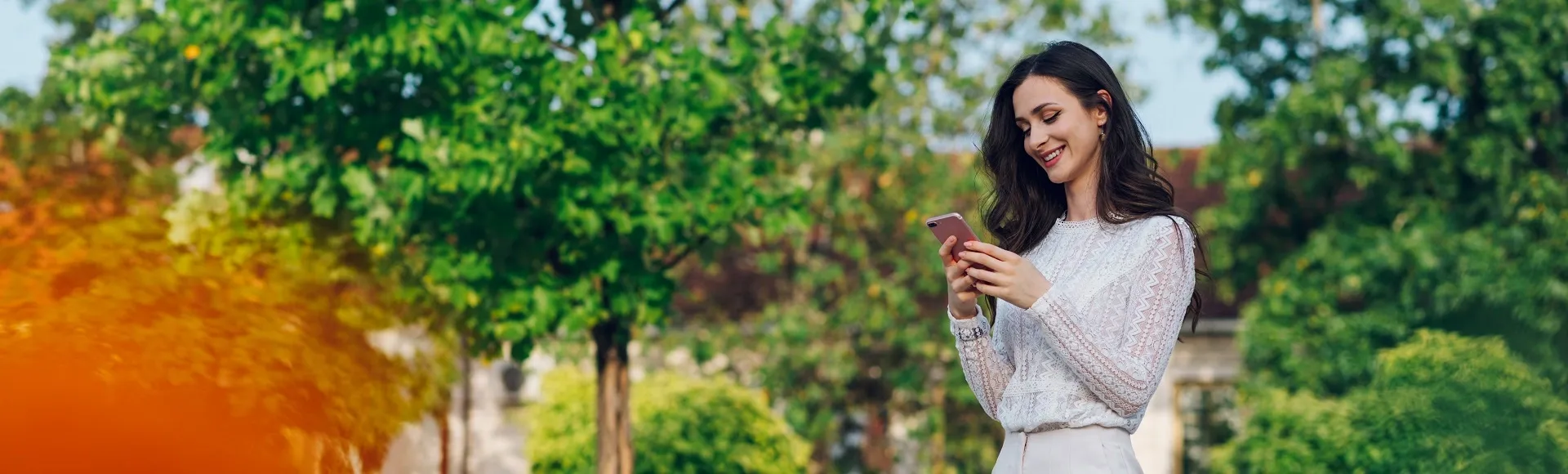 Woman smiling while using a smartphone outdoors in a green park.
