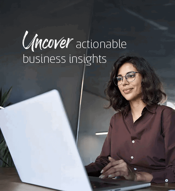 Businesswoman wearing glasses and a brown blouse working on her laptop in a modern office with glass walls.