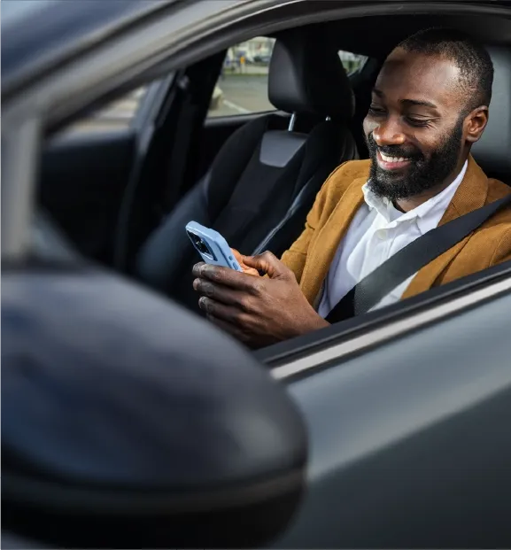 Smiling man using a smartphone while sitting in a parked car.