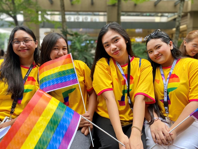 Four TP employees in yellow shirts holding rainbow Pride flags