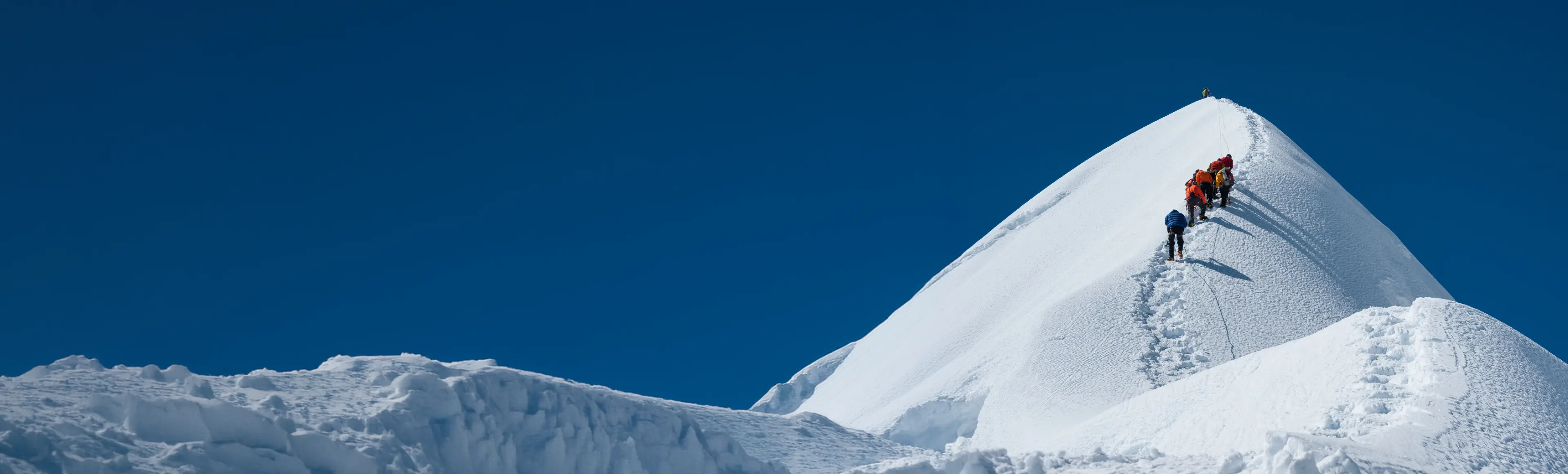 TP team climbing a snow-covered mountain ridge under a clear blue sky.
