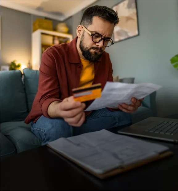 Man reviewing a bill while holding a credit card at home.