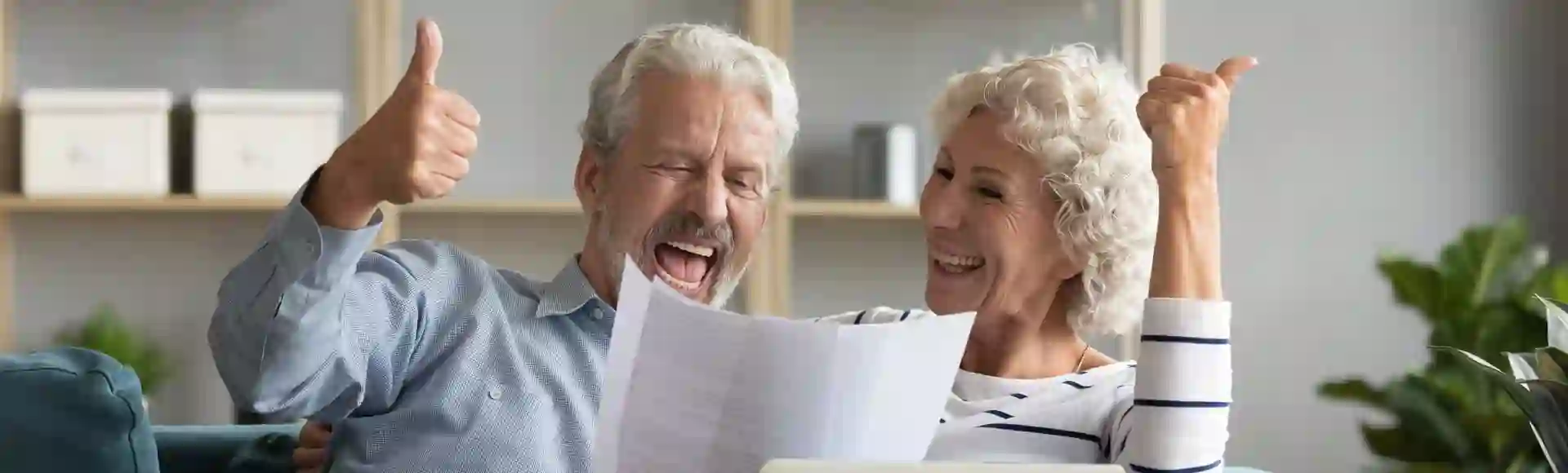 Happy elderly couple celebrating while reviewing a document on a laptop at home.