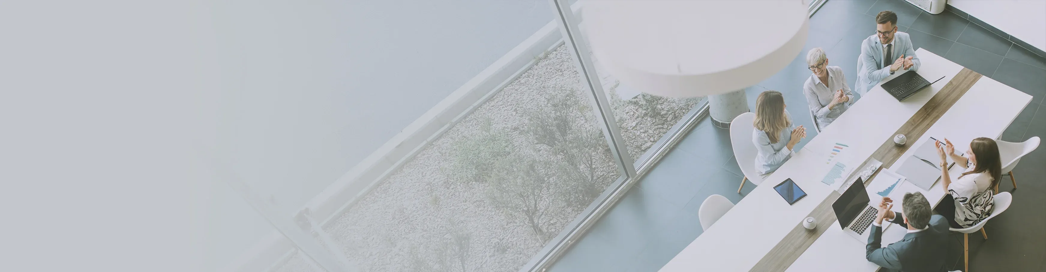 A team of business professionals claps together around a conference table, celebrating a successful meeting or milestone in a bright modern office. 