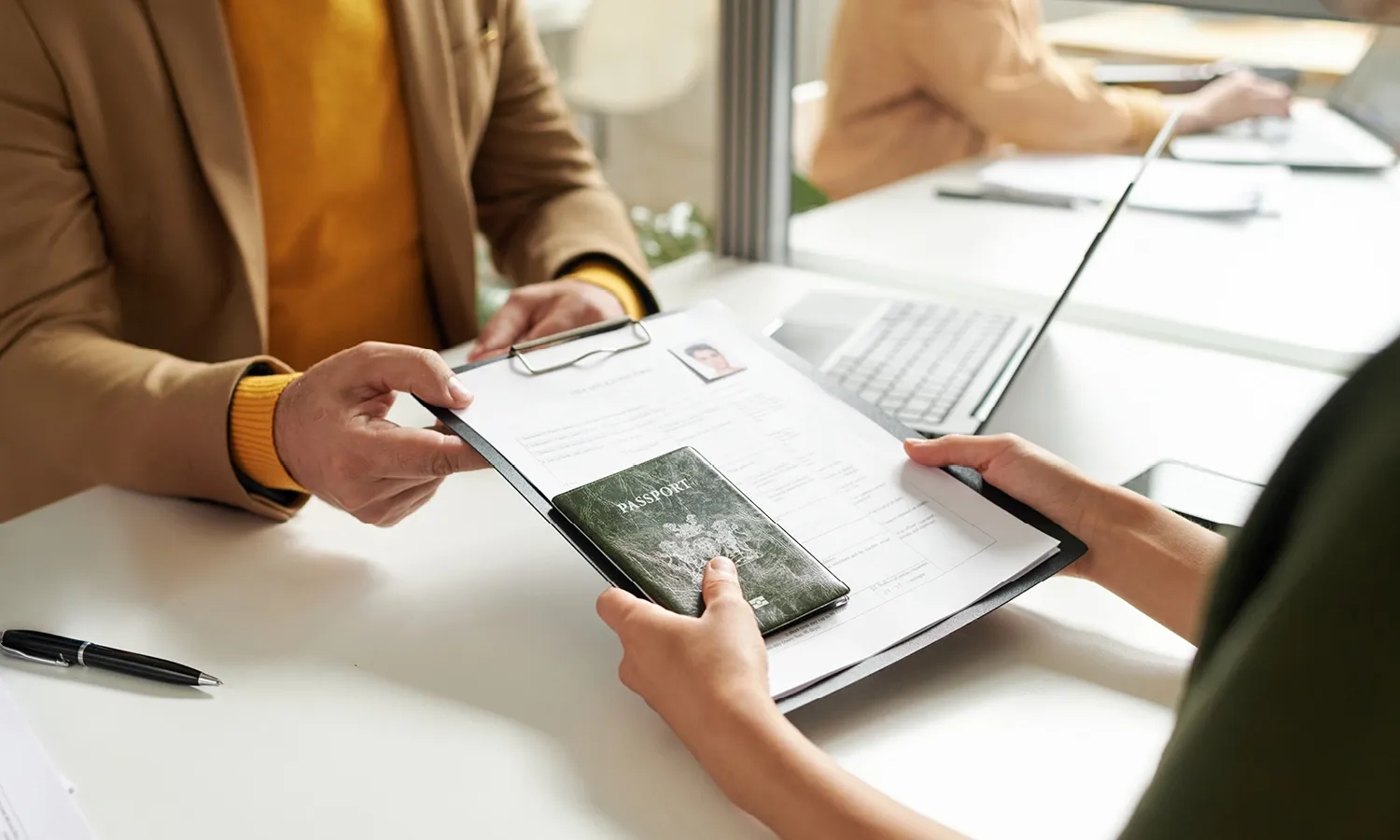Person handing over a passport and documents during a visa application process.