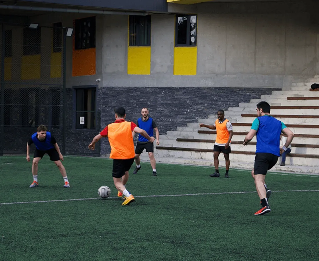 TP employees play soccer on a field outside a building with colorful windows.