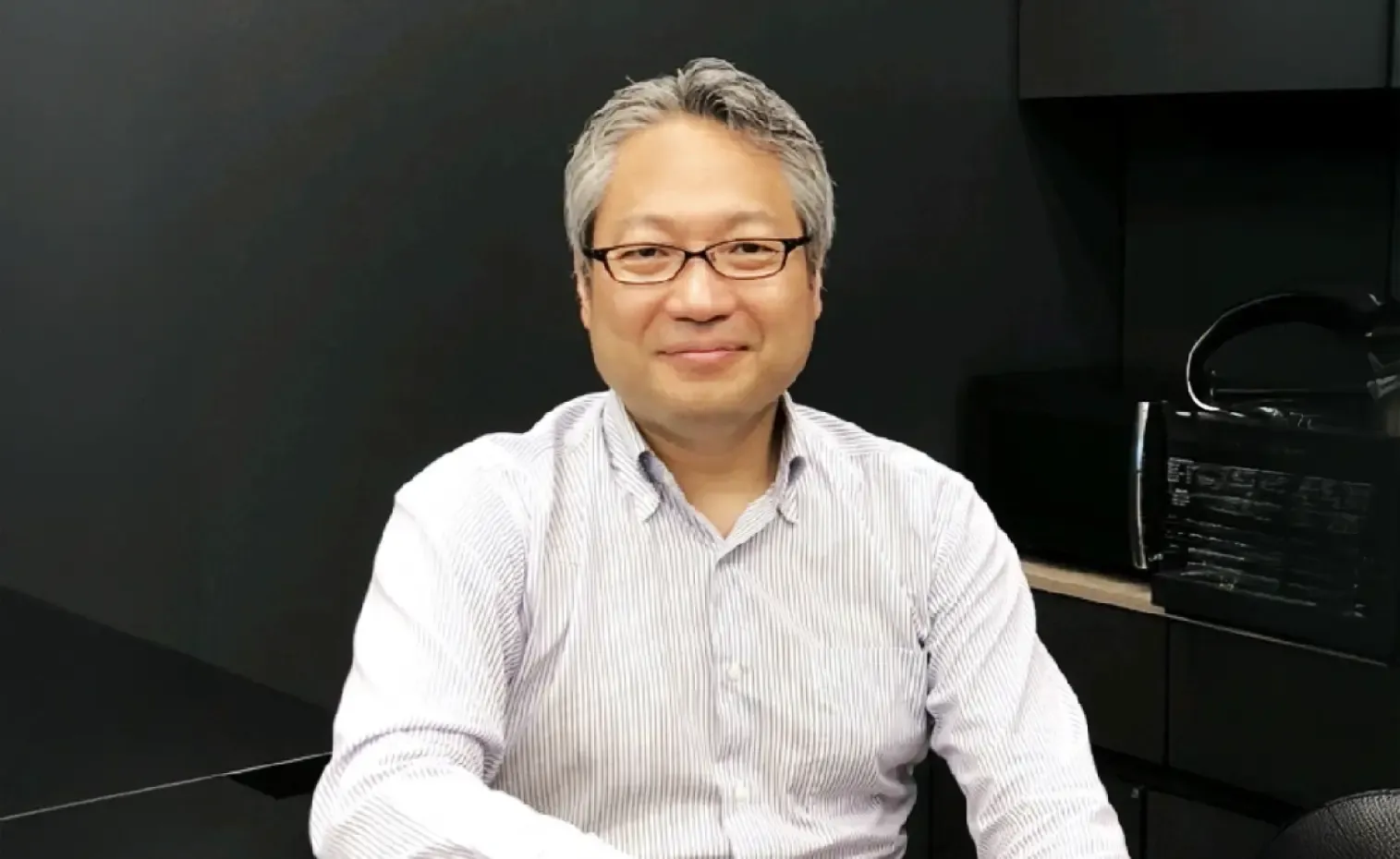 A short-haired, bespectacled young man in a striped shirt