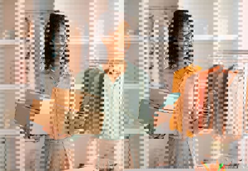 Retail and e-commerce businesswoman smiling confidently while holding boxes and her phone.