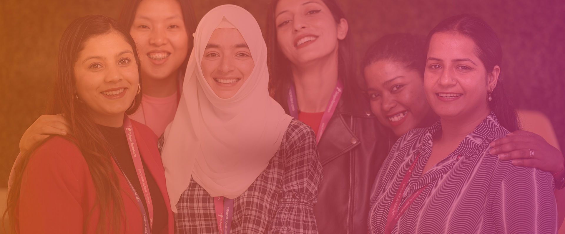A group of six women smiling, standing close together in a warmly lit space, creating a friendly, supportive atmosphere.