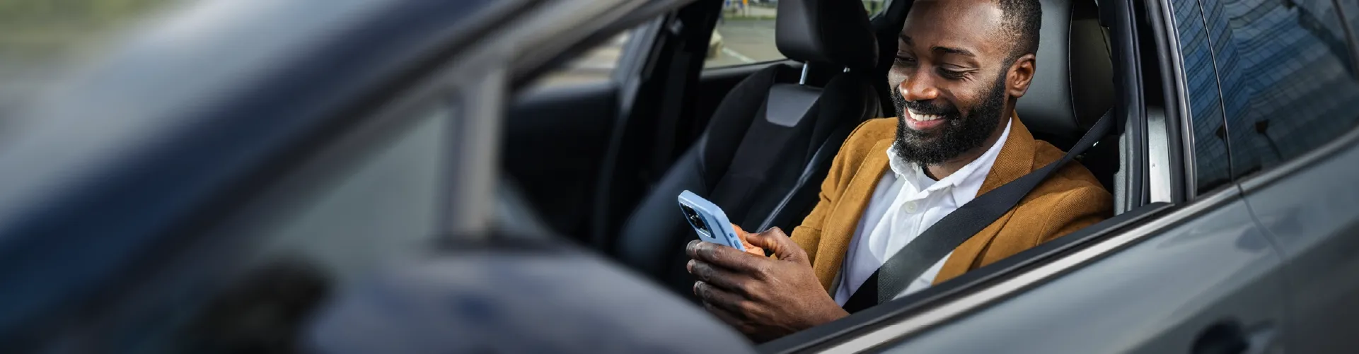 Smiling man using a smartphone while sitting in a parked car.