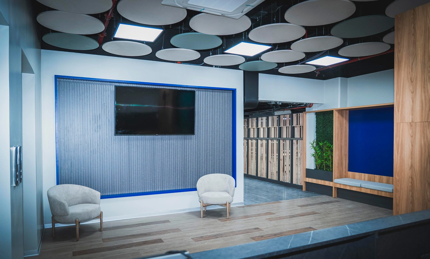 Modern office lounge with seating area and wall-mounted TV display.