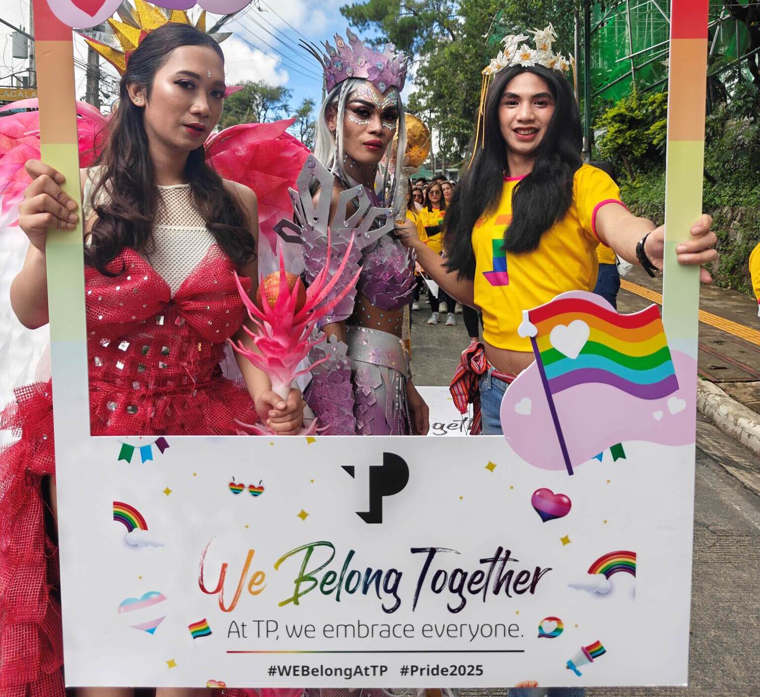 Three TP Pride participants posing with decorative event frame and rainbow flags