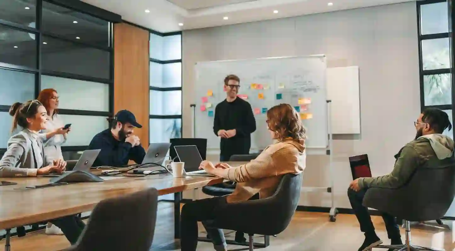 Young and diverse team having a meeting in a modern and comfortable space with a large wooden table in the center and a scrum board in the background