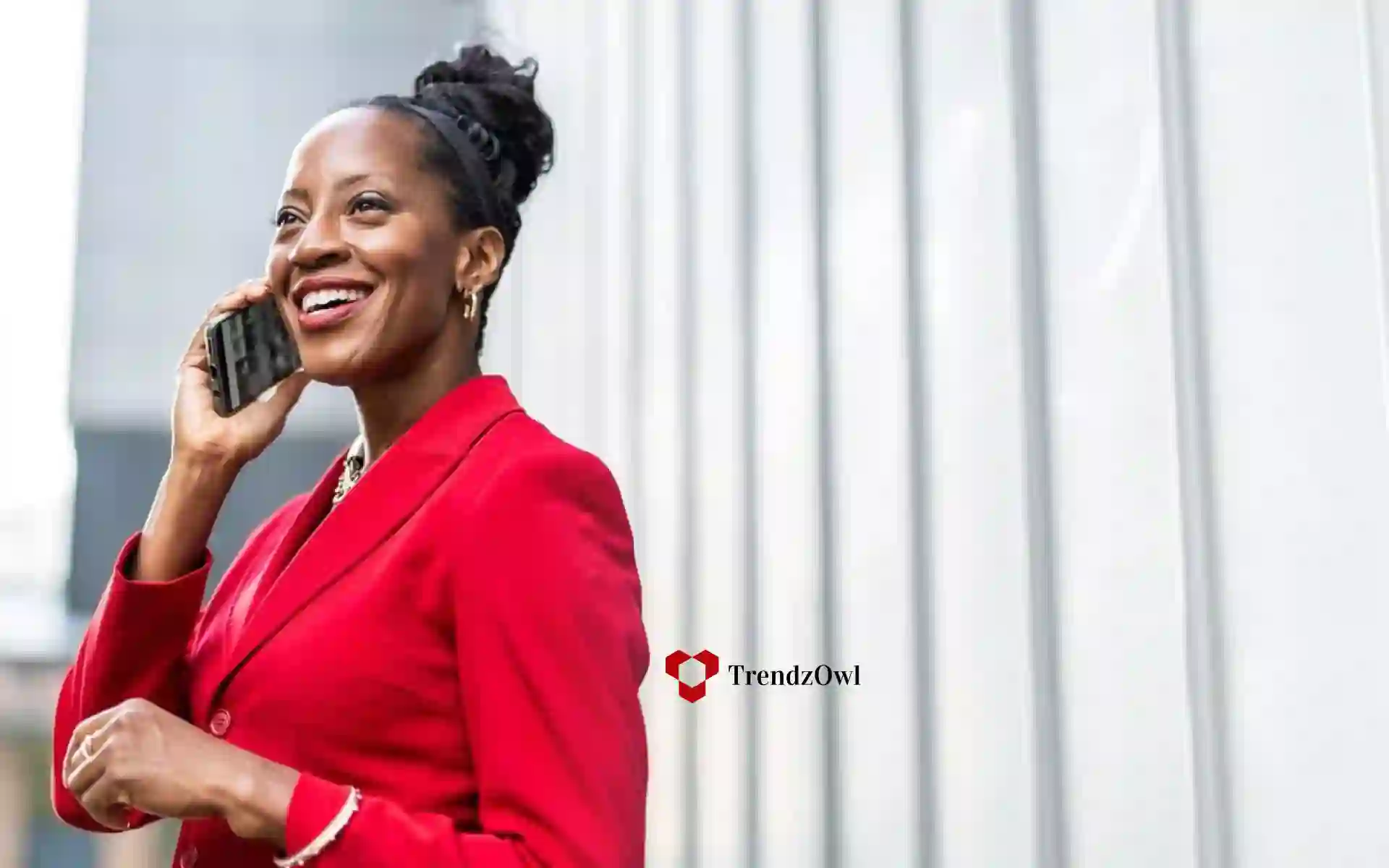 African businesswoman wearing a red blouse smiles while talking on the phone.