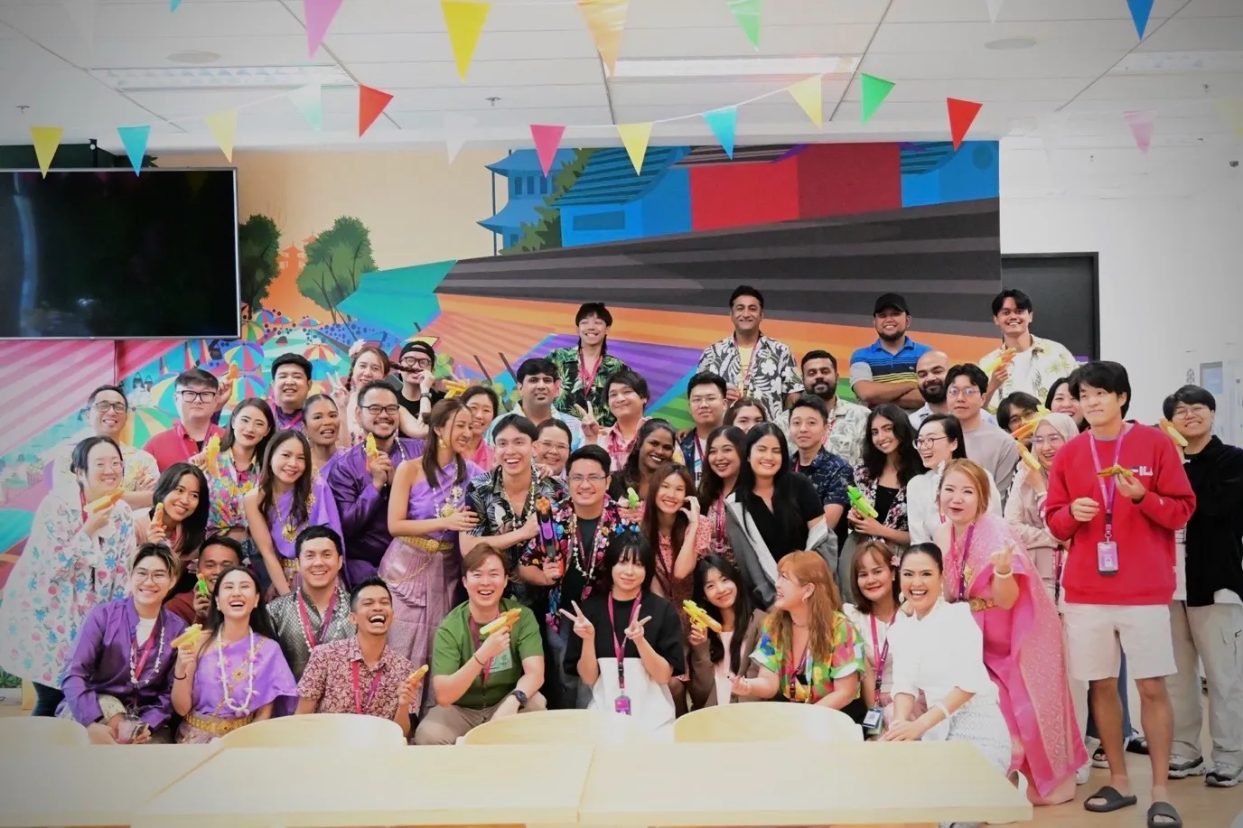 A diverse group of colleagues gathers joyfully, celebrating together in vibrant, cultural attire at a lively office event.