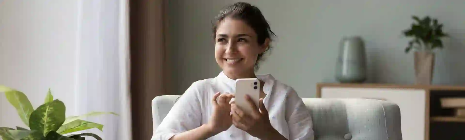 Woman sitting comfortably on her sofa, using her smartphone. The image illustrates a blog about empathy-driven and optimized debt recovery.