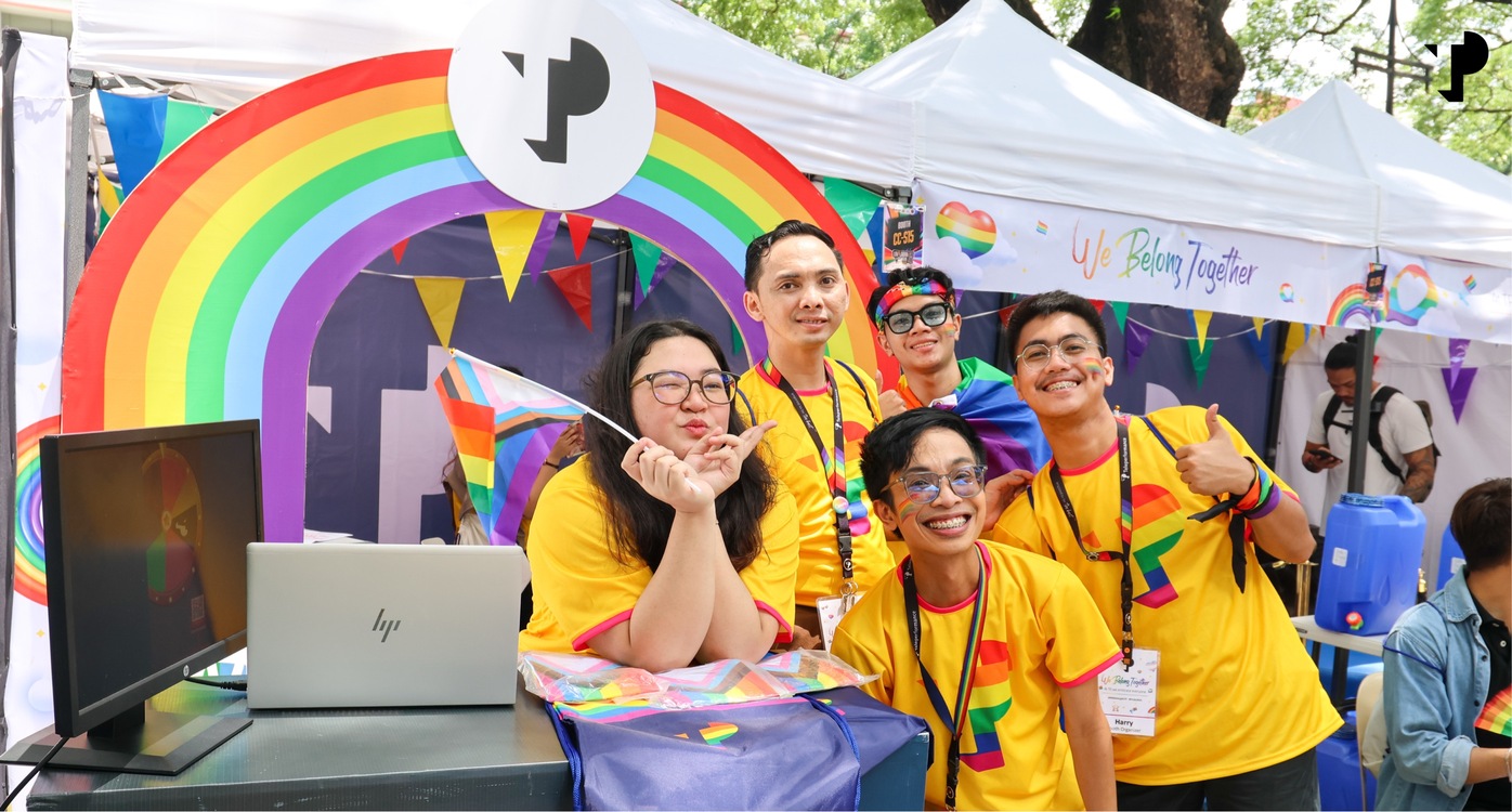 Five TP employees smiling at Pride event booth with rainbow decorations