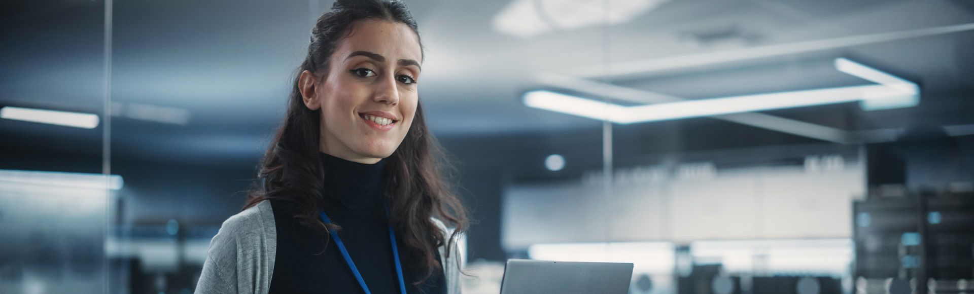 Young female data services employee smiling with her hair tied back and wearing a badge, representing a blog on demystifying cloud-as-a-service from architecture to offerings.