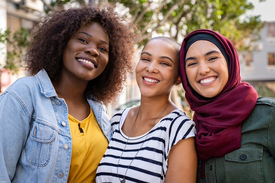Three young women from diverse backgrounds smiling together.