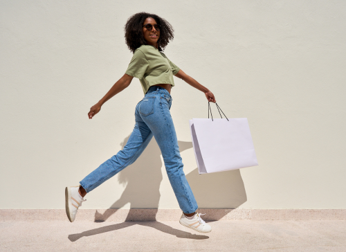 Smiling young Afro-descendant woman carrying shopping bags on a brightly lit street, conveying energy, confidence, and joy.