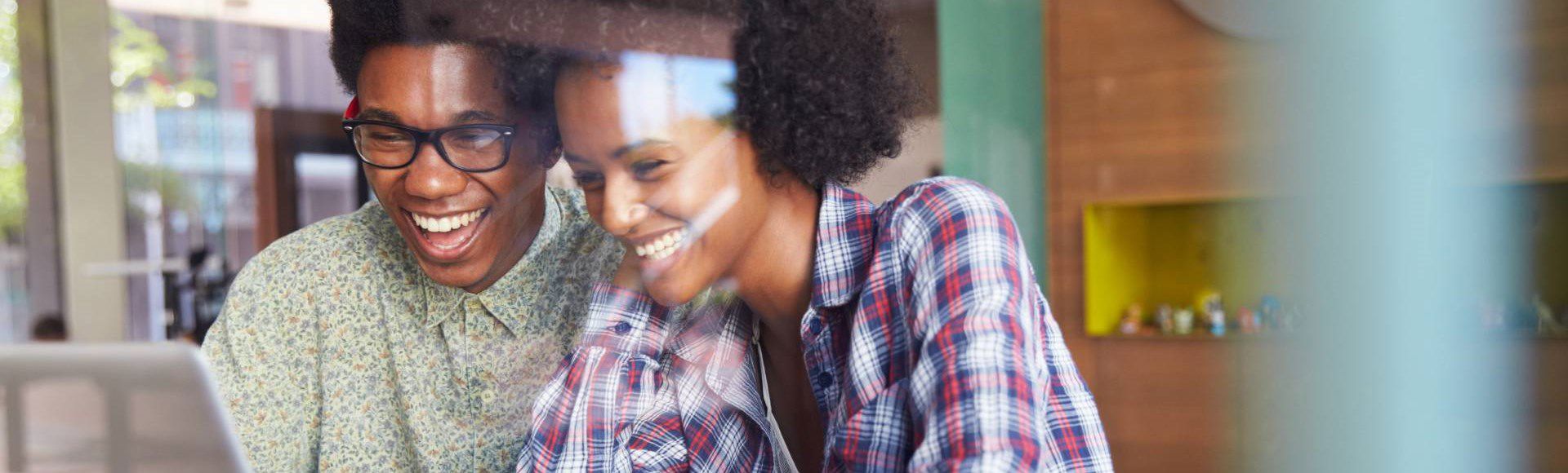 Smiling African couple checking news on a computer together.