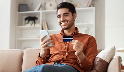 Person sitting on a couch holding a smartphone and a credit card, engaging in online payment.