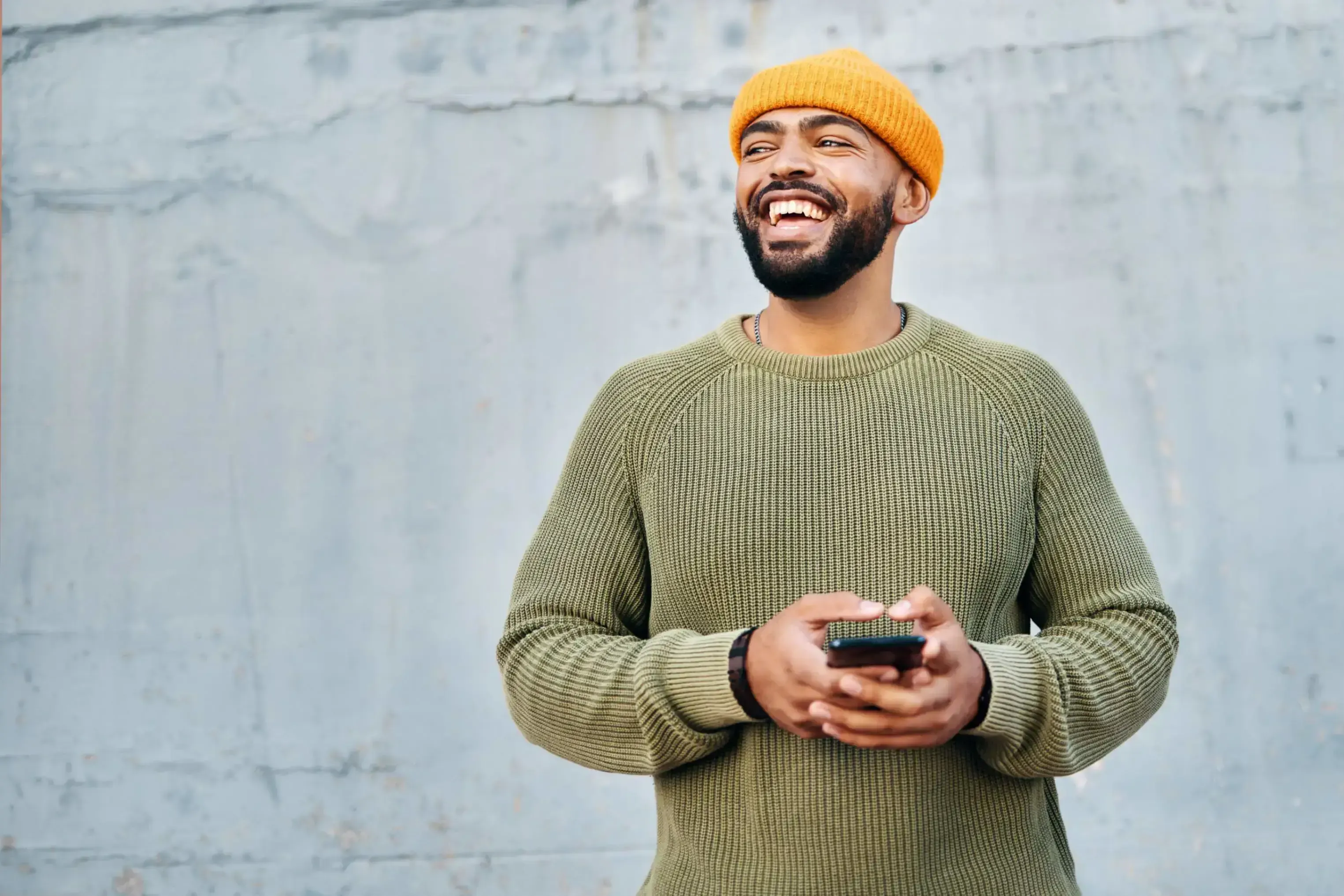 Smiling man in a beanie holding a phone, representing TP’s focus on connection and positive experiences.