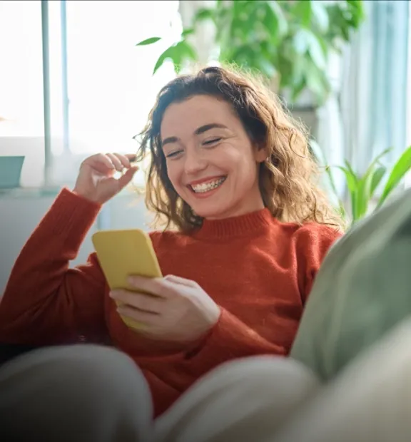 Smiling woman sitting comfortably on her sofa and browsing her cellphone