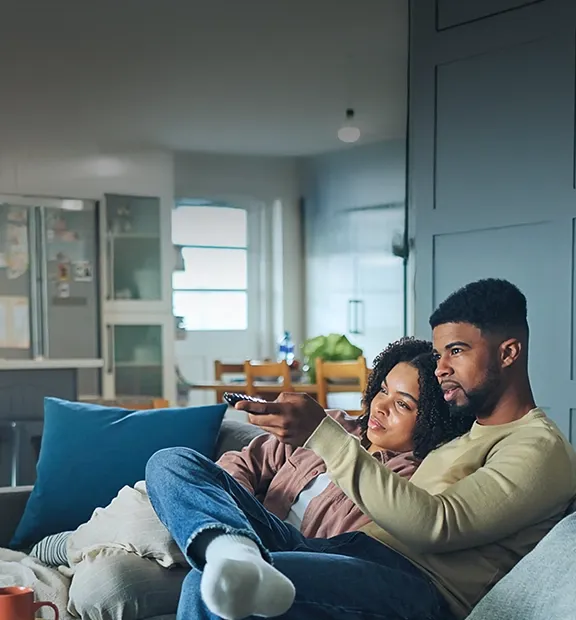 Couple watching television together while sitting comfortably on a sofa at home.