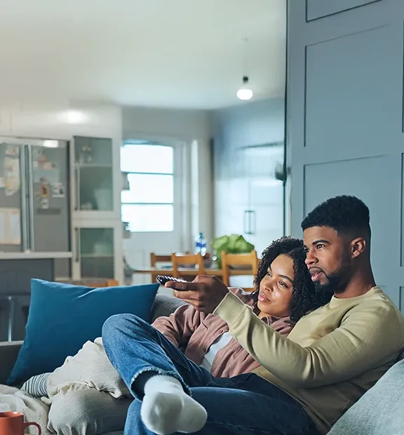 Couple watching television together while sitting comfortably on a sofa at home.