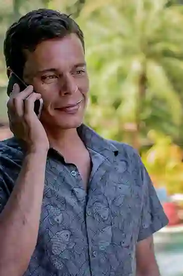 Man in patterned shirt smiling while talking on a mobile phone outdoors.