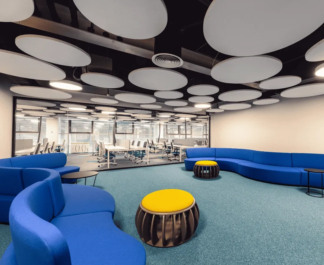 ლურჯი მოდულური სავარძლები ნახევარ წრეში ყვითელი პუფებით თანამედროვე ოფისის ლაუნჯში.